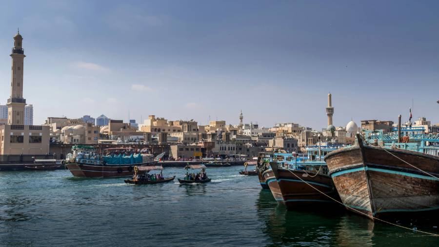 Traditional wooden boats on the water at Dubai Marina, with low-rise buildings and a mosque minaret in the background