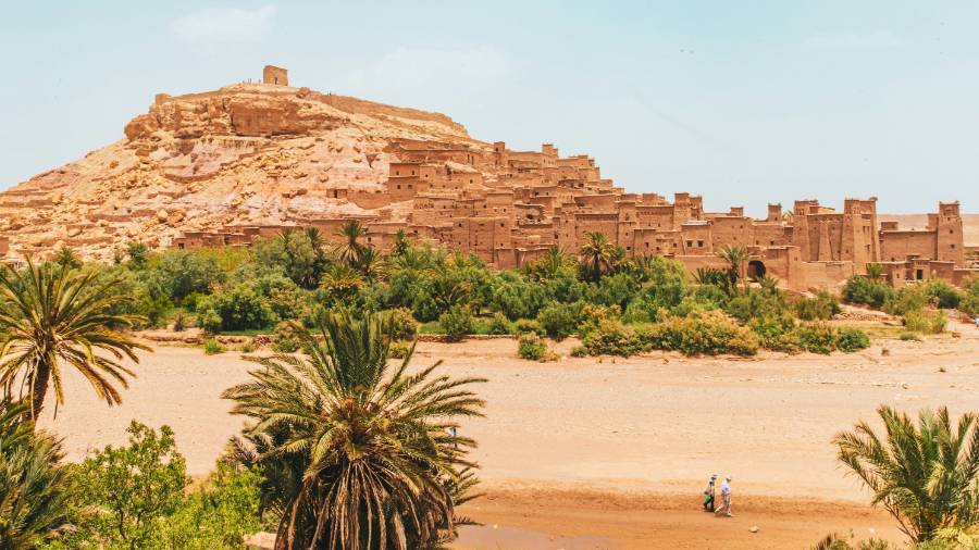 People walking on brown sand near brown rock formation during daytime