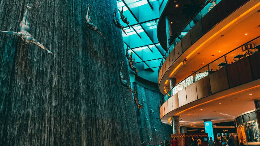 The Dubai Waterfall inside Dubai Mall, with metallic sculptures of divers, set in a multi-level space with glass ceilings and people below