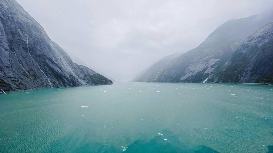 an expanse of turquoise water with floating ice between steep, misty mountains 