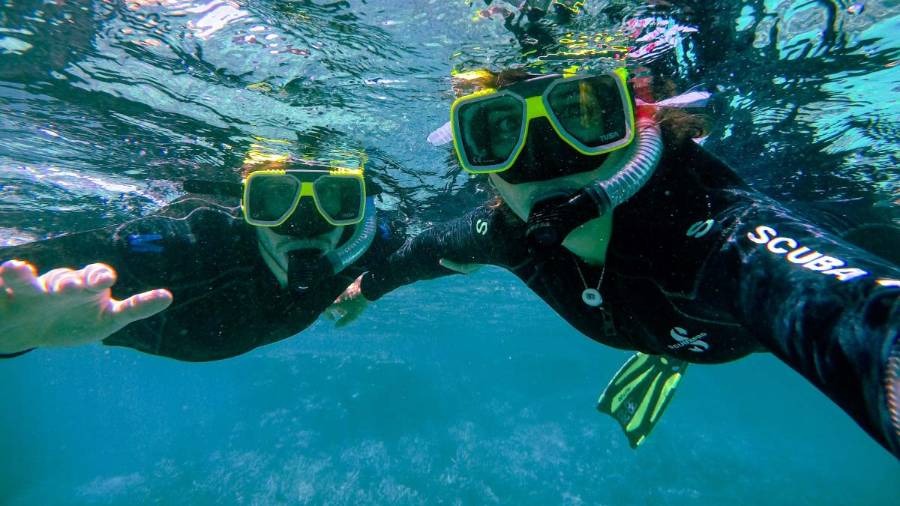 Two people wearing snorkelling gear seen underwater looking at their camera