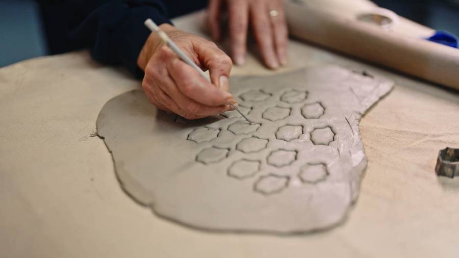 A person’s hands carving hexagonal shapes into a rolled piece of clay on a flat surface