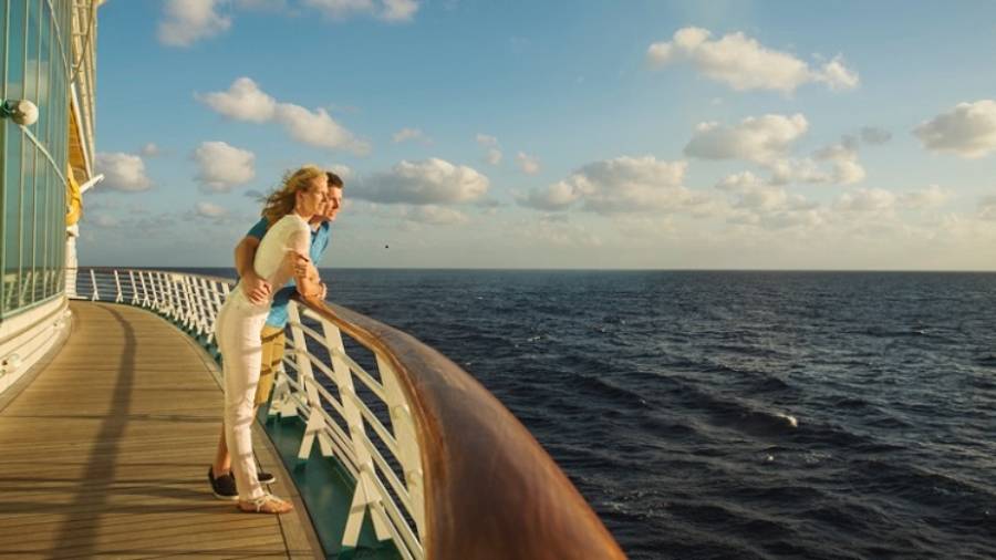 A couple leaning on the railings of a boat, looking out to sea
