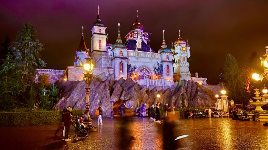 Fairytale-style castle lit up at night with glowing lamps and visitors walking by