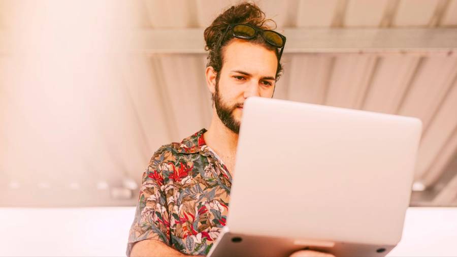 Person in a floral shirt using a laptop on a day bed while on holiday