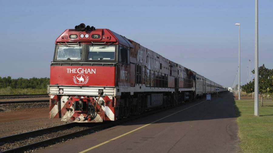 A red and white train travelling down train tracks with the words “The Ghan” on the front of the engine