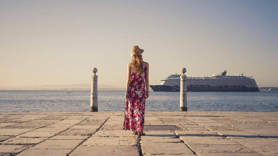 New York City skyline view from the pavemaA person stands near the sea with a cruise ship and stone pillars in view ent featuring the art deco spire of the Chrysler building