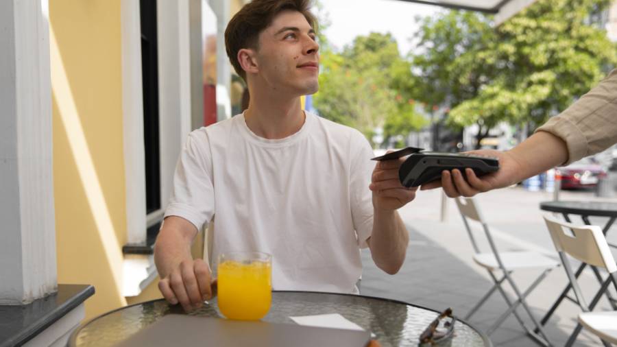 A person sitting at a table outside tapping their card on a card machine to pay