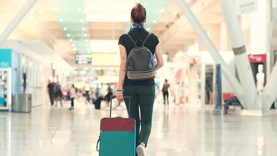 Woman wearing backpack walking at the airport pulling wheeled luggage behind her