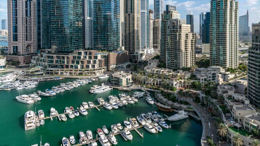 Aerial view of Dubai Marina with yachts in turquoise water, surrounded by modern high-rise buildings and waterfront greenery