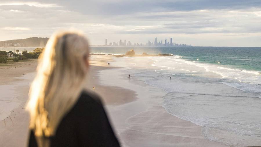 A person sitting on a beach looking at a city through the spray of the ocean waves. Gold Coast, Queensland, Australia 