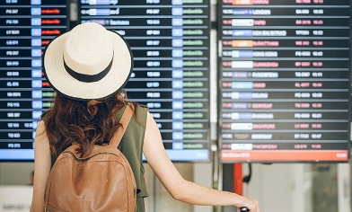 Woman wearing hat and backpack at airport looking a departure board at the airport