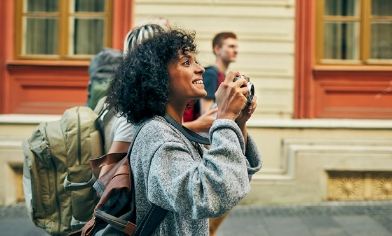 Woman wearing backpack holding a camera taking a photo in a street