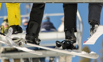 Skier legs and boots in skis on a ski lift with other ski lifts with skiers in them in background