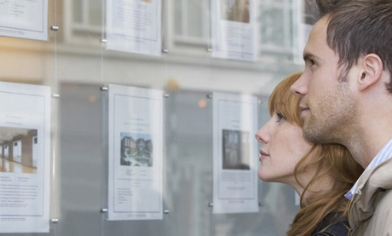 Young couple looking at house listings in estate agent (window)