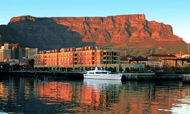 A white cruiser sits in the sunset-lit waters of Cape Town harbour, with the famous Table Mountain in the background