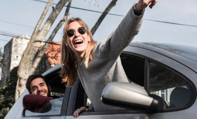 Two people hanging out of the window of a parked car and pointing into the distance