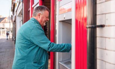 Side view of a man standing at a Post Office branded cash machine outside a branch on a high street