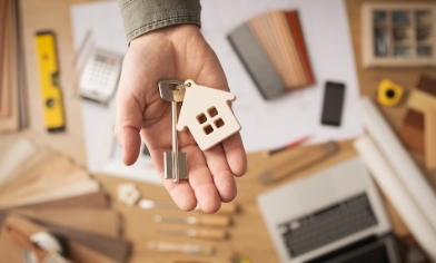 Key with metal house keyring attached, resting inside the palm of a hand above a work bench