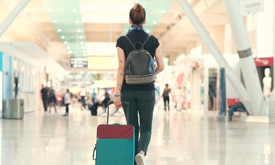 Woman wearing backpack walking at the airport pulling wheeled luggage behind her