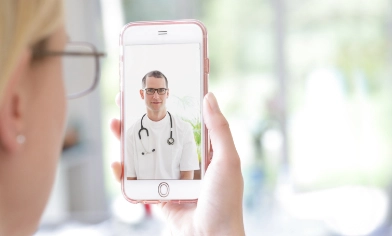 Woman holding up mobile phone, showing a doctor on the screen