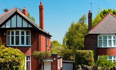 Semi-detached houses on a road surrounded by trees and bushes beneath clear blue skies