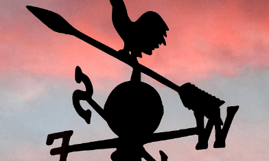 Weather vane silhouette, with arrows and letters for North, South, East and West under sunset sky