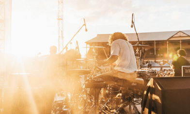 Drummer and band playing music to a crowd with sun in background