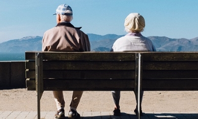 Elderly couple sitting on a bench looking out to sea with mountains in background