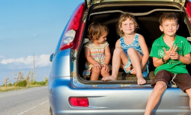 Three happy smiling kids sitting in the back of a car