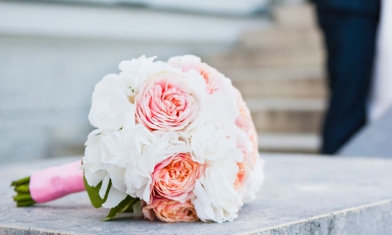 Wedding bouquet with pink and white roses, sat on stone stair bannister, bride & groom in distance