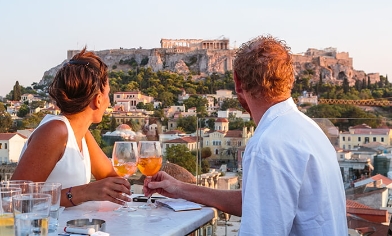 Couple dining outdoors in Athens holding wine glasses looking out to ruins