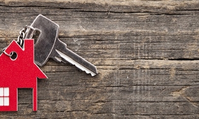 Key with red house key ring attached with chain laying on wooden surface