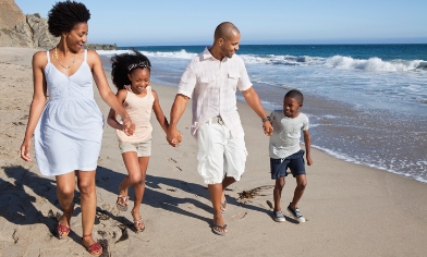 Young family of four walking along a sandy beach with waves to their left