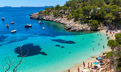 Rocky and green coastline with people on sandy beach surrounded with blue waters and boats