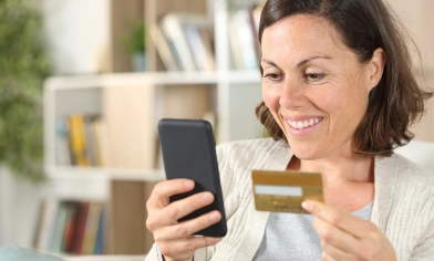 a customer smiling and looking at her phone whilst holding a credit card