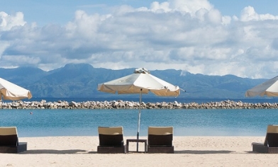 Sun loungers and parasols on sandy beach pointing toward the sea and distant mountains