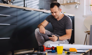 Man kneeling down on one knee looking at his phone with DIY tools in front of him