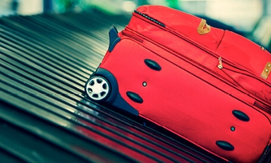 Red suitcase on airport conveyor belt at luggage reclaim