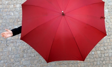 Person on cobble street under an open red umbrella holding their hand out to feel the rain