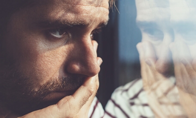 Bearded man leaning on hand looking out of a window in to distance
