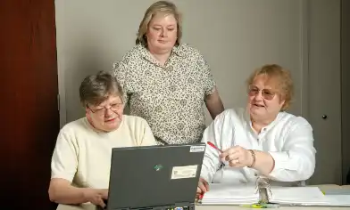 Three adults reviewing a binder of papers in front of an open laptop