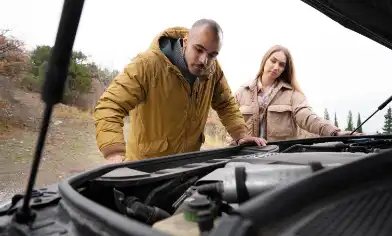 A couple stands by the open bonnet of a presumably broken-down car, looking down at the engine inside