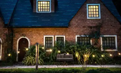 two storey pitched roof house at night with light in the upper windows and in the garden