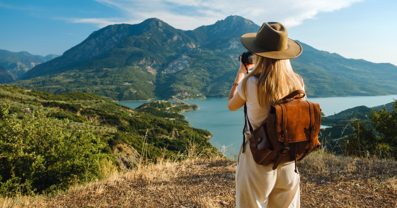 Woman taking picture of landscape featuring a mountain range and lake.