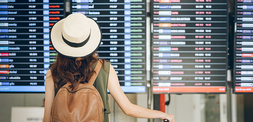 Woman wearing hat and backpack at airport looking a departure board at the airport