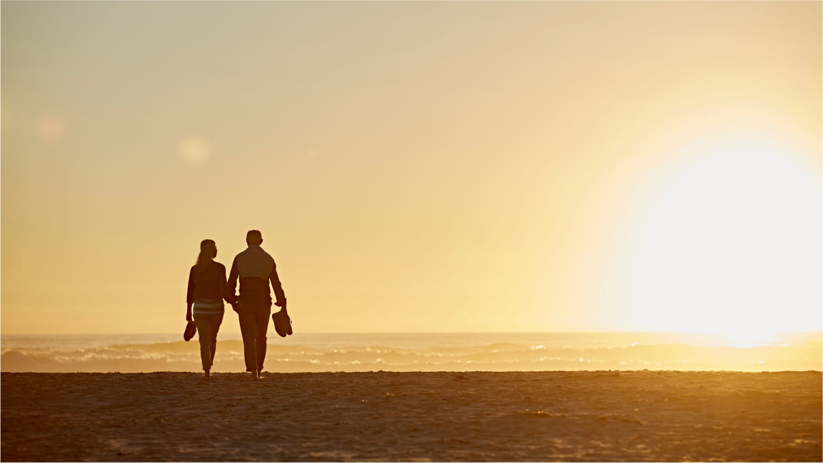 Two people walking on the beach under the sunset