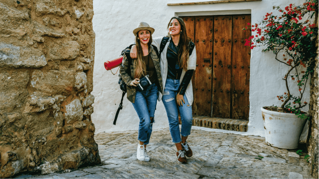Two smiling women tourists, arms around each other's shoulders, walk along an old town street