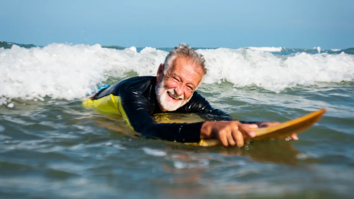 Older man smiling while lying on a surfboard in the sea with small waves