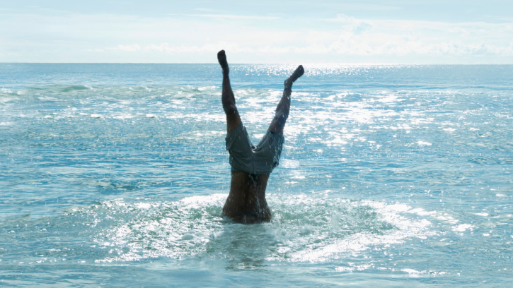 mans legs sticking up as he dives into the blue surf
